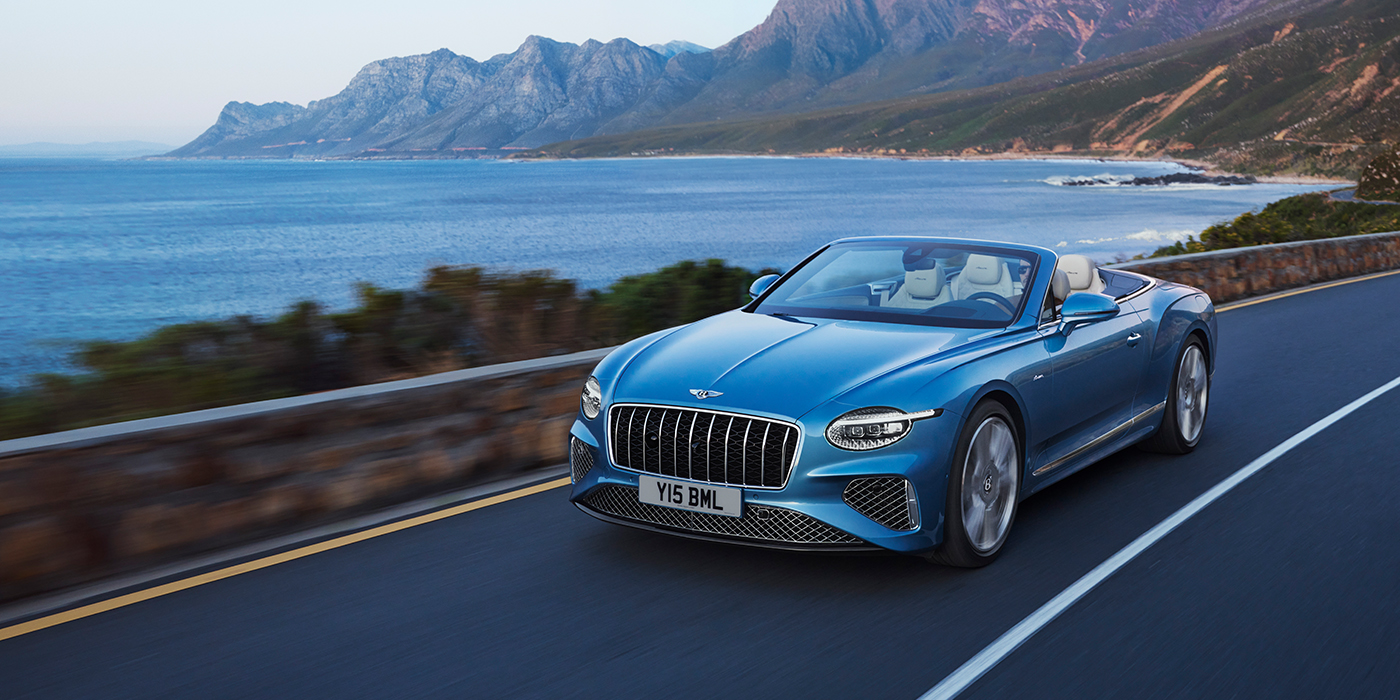 Bentley Riga New Bentley Continental GTC Azure convertible in Light Windsor blue paint with 22 inch Azure wheels and chrome grill, driving dynamically by the sea