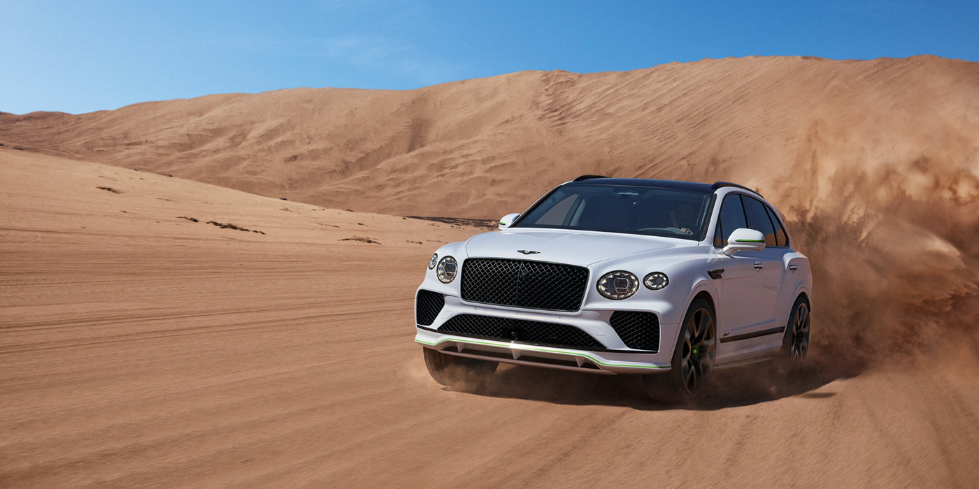 Bentley Riga Bentley Bentayga Speed SUV front three quarter in Snow Quarts Pearlescent by Mulliner white paint driving dynamically through the desert