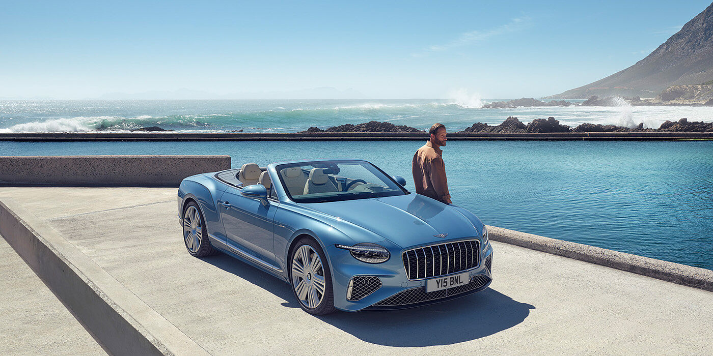 Bentley Riga New Bentley Continental GTC Azure convertible front view in Light Windsor blue paint with 22 inch ten spoke wheels parked by the sea in the sunshine