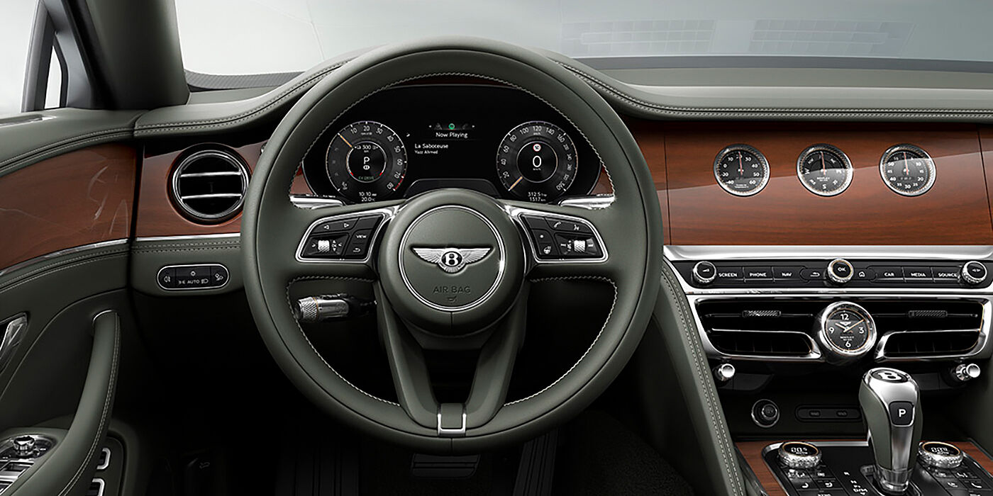 Bentley Riga New Bentley Flying Spur sedan front cabin in Cumbrian Green hide and Crown Cut walnut veneer showing steering wheel and Rotating Display with three clocks on face