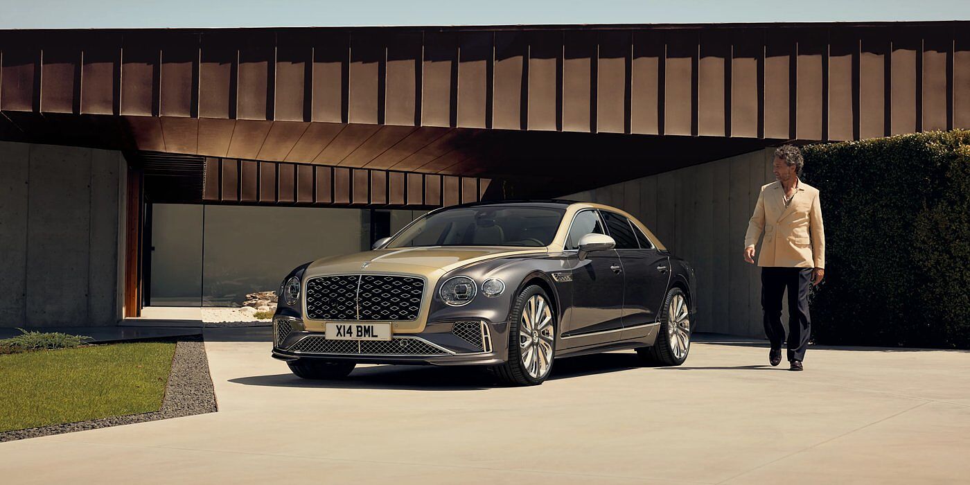 Bentley Riga Bentley New Flying Spur Mulliner V8 hybrid sedan front three quarters in Rose Gold over Magnetic paint, parked near modern home