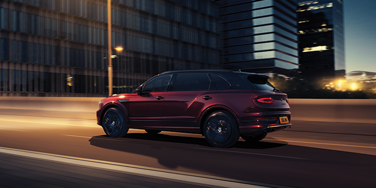 Bentley Riga Bentley Bentayga Extended Wheelbase Mulliner SUV in Cricket Ball red paint driving dynamically in city at night